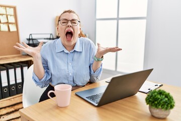 Sticker - Young redhead woman working at the office using computer laptop celebrating mad and crazy for success with arms raised and closed eyes screaming excited. winner concept