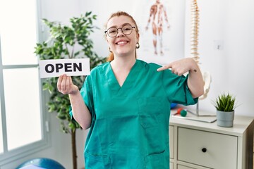 Sticker - Young redhead physiotherapist woman working at pain recovery clinic holding open banner pointing finger to one self smiling happy and proud