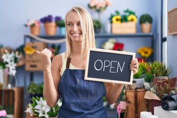 Canvas Print - Young caucasian woman working at florist with open sign pointing thumb up to the side smiling happy with open mouth