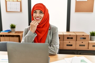 Young woman wearing arabic scarf using laptop working at office