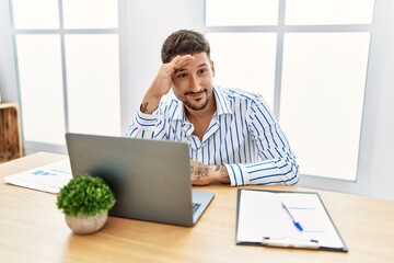 Sticker - Young handsome man with beard working at the office using computer laptop very happy and smiling looking far away with hand over head. searching concept.