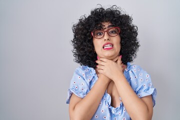 Poster - Young brunette woman with curly hair wearing glasses over isolated background shouting and suffocate because painful strangle. health problem. asphyxiate and suicide concept.