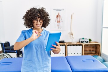 Wall Mural - Young middle east woman wearing physio therapist uniform having video call at clinic