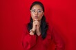 © Krakenimages.com - Asian young woman standing over red background looking fascinated with disbelief, surprise and amazed expression with hands on chin