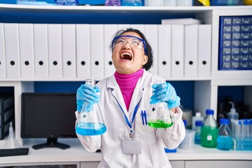 Canvas Print - Young asian woman working at scientist laboratory angry and mad screaming frustrated and furious, shouting with anger looking up.