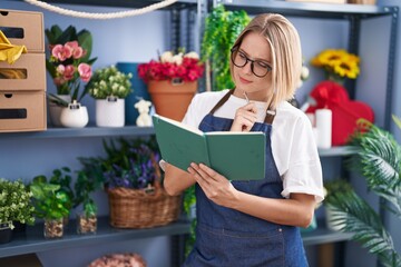 Young blonde woman florist writing on notebook with doubt expression at florist shop