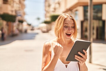 Wall Mural - Young blonde woman smiling confident using touchpad at street