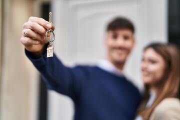 Mand and woman couple hugging each other holding key of new home at street