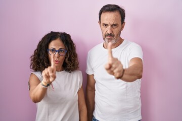 Sticker - Middle age hispanic couple together over pink background pointing with finger up and angry expression, showing no gesture