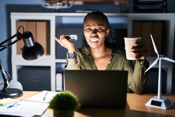 Canvas Print - African woman working using computer laptop at night pointing aside worried and nervous with forefinger, concerned and surprised expression