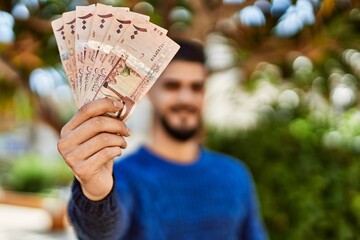 Young arab man smiling confident holding riyal banknotes at park