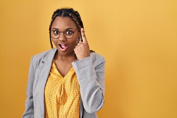 Poster - African american woman with braids standing over yellow background pointing finger up with successful idea. exited and happy. number one.