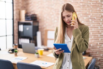 Wall Mural - Young caucasian woman business worker using touchpad talking on smartphone at office