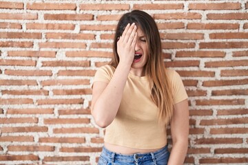 Poster - Young brunette woman standing over bricks wall yawning tired covering half face, eye and mouth with hand. face hurts in pain.