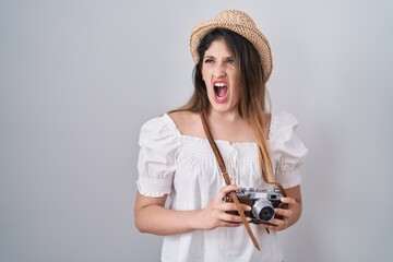 Sticker - Young brunette woman holding vintage camera angry and mad screaming frustrated and furious, shouting with anger. rage and aggressive concept.