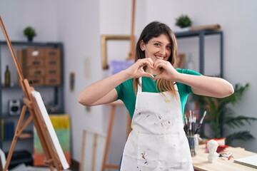 Sticker - Young brunette woman at art studio smiling in love doing heart symbol shape with hands. romantic concept.