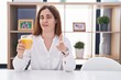 © Krakenimages.com - Brunette woman drinking glass of orange juice pointing fingers to camera with happy and funny face. good energy and vibes.