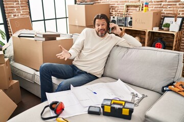 Wall Mural - Handsome middle age man moving to a new home speaking on the phone celebrating achievement with happy smile and winner expression with raised hand