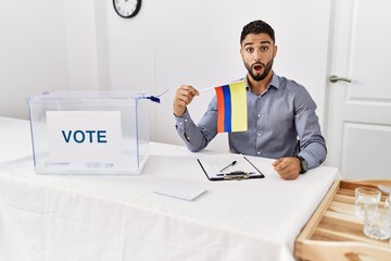 Sticker - Young handsome man with beard at political campaign election holding colombia flag scared and amazed with open mouth for surprise, disbelief face