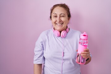 Sticker - Senior woman wearing sportswear and headphones winking looking at the camera with sexy expression, cheerful and happy face.