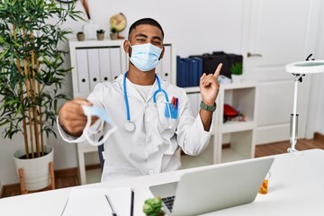 Wall Mural - Young indian doctor offering safety mask smiling happy pointing with hand and finger to the side