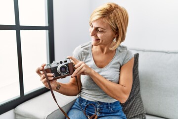 Sticker - Middle age blonde woman smiling confident holding vintage camera at home