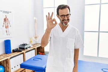 Poster - Middle age man with beard working at pain recovery clinic smiling positive doing ok sign with hand and fingers. successful expression.