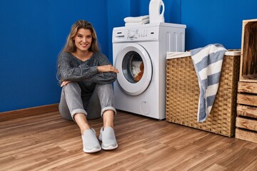 Wall Mural - Young blonde woman sitting on the floor waiting for washing machine at laundry room