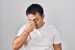 © Krakenimages.com - Young chinese man standing over white background tired rubbing nose and eyes feeling fatigue and headache. stress and frustration concept.
