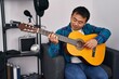 © Krakenimages.com - Young chinese man guitarist playing classical guitar at music studio
