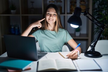 Wall Mural - Teenager girl doing homework at home late at night smiling cheerful showing and pointing with fingers teeth and mouth. dental health concept.