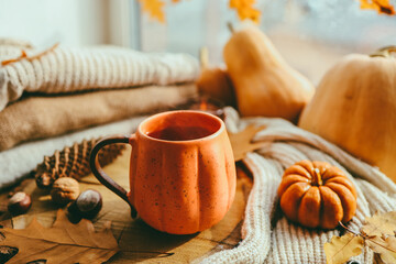 A cup of hot steaming tea and a pumpkin-shaped candle on the windowsill, autumn mood