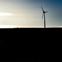 single wind turbine in silhouette at twilight, set on a small hill on a farm in scotland. the scotti