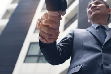 Asian businessmen making handshake with office building as background,  business etiquette, congratulation, merger and acquisition, business meeting and partnership concepts