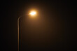 © TRAVELARIUM - One night lamppost shines with faint mysterious yellow light through evening fog. Streetlight shine at quiet city night, magic atmospheric light in mystical darkness, copy space