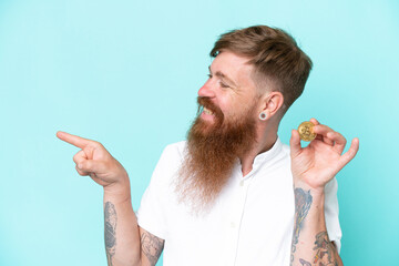 Wall Mural - Redhead man with long beard holding a Bitcoin isolated on blue background pointing to the side to present a product