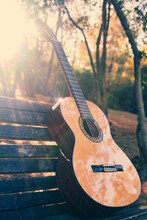 Beautiful Classical Guitar On A Bench In The Park With Lens Flare. Photo Of A New Wooden Guitar With Nylon Strings Outdoors In The Summer During Sunset. No People. Beautiful String Instrument.