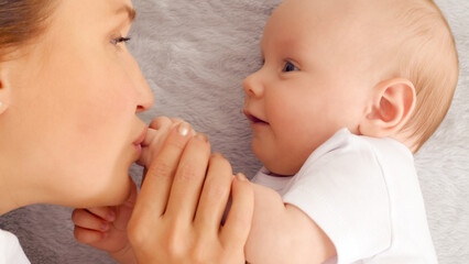 Wall Mural - Happy newborn baby with his mother. Healthy newborn baby in a white t-shirt with mom. Closeup Faces of the mother and infant baby. Cute Infant boy and parent, top view. Happy family portrait