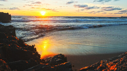 Poster - Beautiful natural landscape with sandy beach  with big stones during sunset.  Sun over horizon and Rolling ocean waves to the rocky shore while sunset.  Summer tourist destination in Portugal. Travel