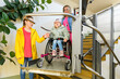 Mother with a young child living with cerebral palsy using electric wheelchair lift to access public building. Special lifting platform for wheelchair users. Disability stairs lift facility.