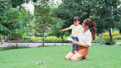 Asian young mother holding a little son of her being irritable in park.