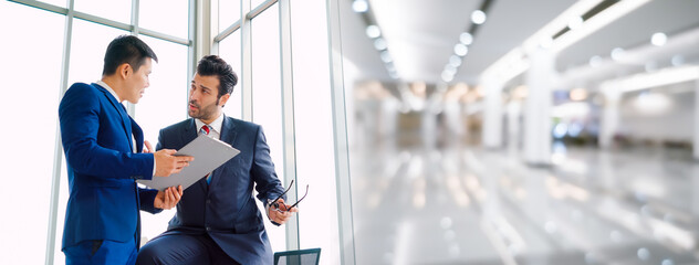 Two business people talk project strategy at office in widen view meeting room. Businessman discuss project planning with colleague at modern workplace .