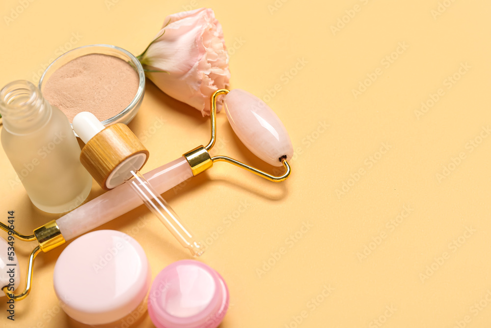 Facial massage tool with cosmetic products and rose on beige background