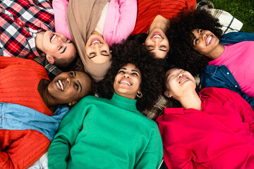 Wall Mural - Happy young multi ethnic women having fun lying on park grass - Diversity and friendship concept