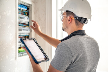 Wall Mural - Man, an electrical technician working in a switchboard with fuses, uses a tablet.