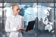 © Who is Danny - Attractive young european businesswoman using laptop and standing in interior with creative map hologram on blurry window with city view. Global business, success and CEO concept.