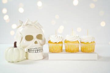 Wall Mural - Halloween product mockup. Party treats cupcakes with white skull pumpkins against a white background with bokeh party lights. Negative copy space.