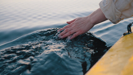 Person dips hand in calm river water sitting in sailing boat