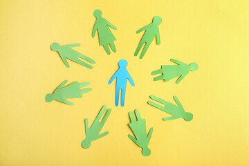 Wall Mural - Circle of green paper human figures with blue one in middle on yellow background, flat lay. Diversity and inclusion concept