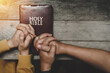 © Deemerwha studio - Top view christian of couple or group people holding hands praying worship together to believe and Bible on a wooden table for devotional for prayer meeting concept.
